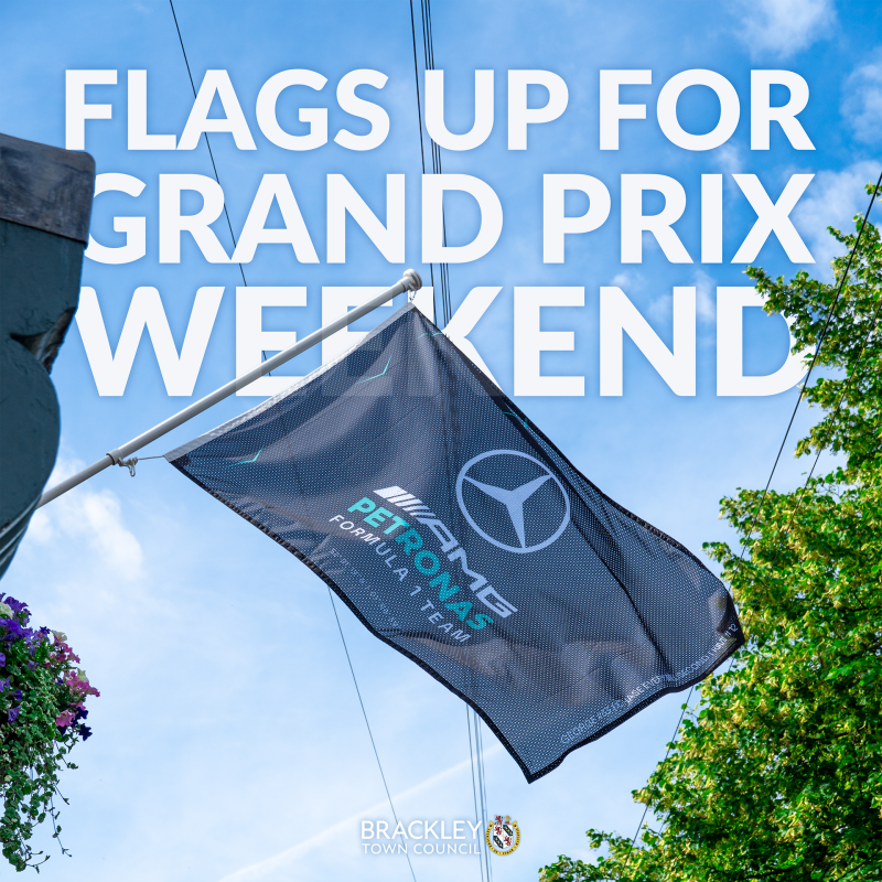 Mercedes-AMG Petronas Formula One Team flag flying above a street in Brackley, with promotional text announcing flags are up for the Silverstone Grand